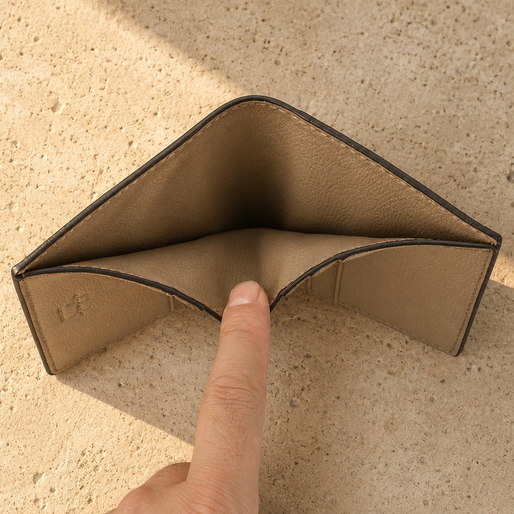 Empty beige wallet on a textured surface with a finger pointing at it