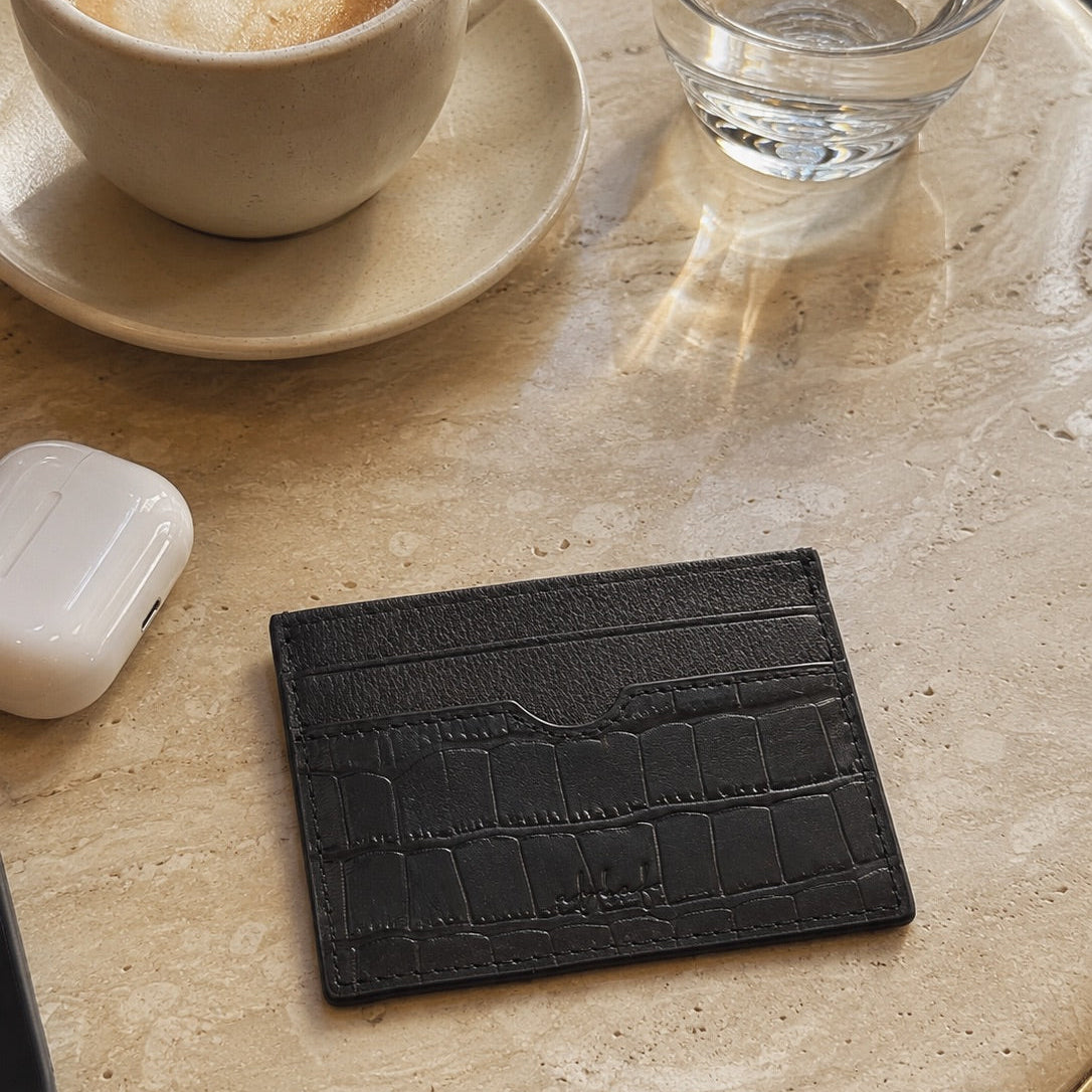 Black textured cardholder on a table with a cup of coffee and a glass of water.