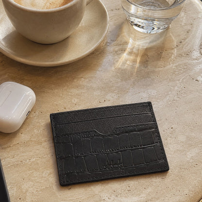 Black textured cardholder on a table with a cup of coffee and a glass of water.