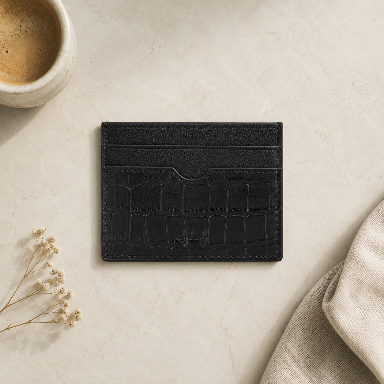 Black cardholder on a light surface with a cup of coffee and dried flowers.